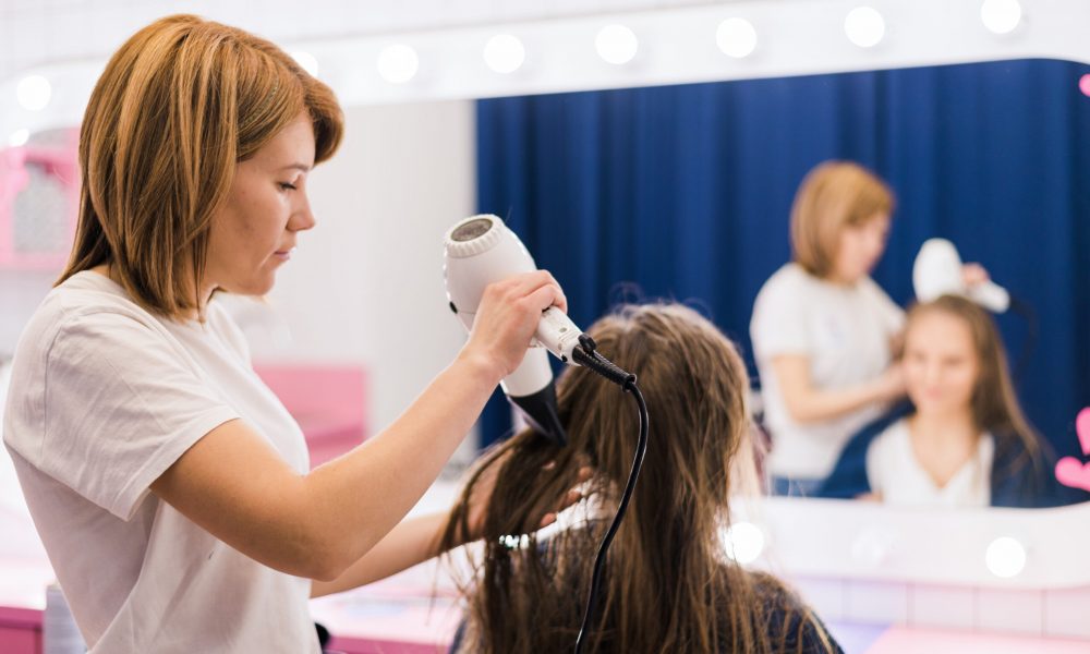 Professional female hairdresser drying woman's hair styling using blow dryer at the hairdressing saloon